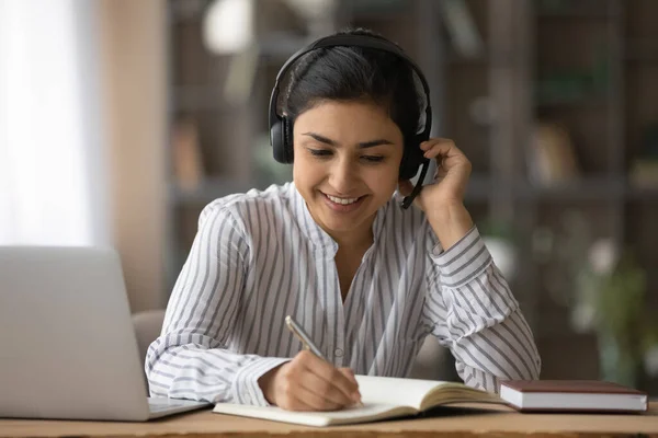 Close up smiling Indian woman in headphones taking notes, studying — Stock Photo, Image