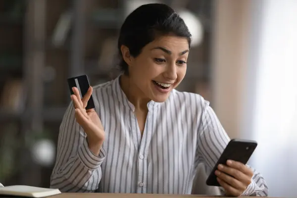 Cerca de la mujer india emocionada sosteniendo la tarjeta de crédito, usando smartphone — Foto de Stock