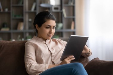 Tablet kullanan Hintli kadın, evdeki koltukta oturuyor.