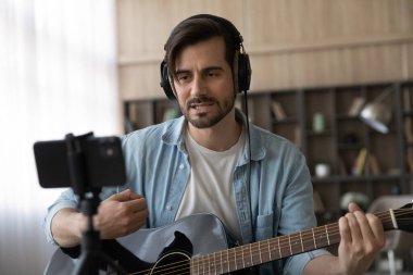 Kulaklıklı adam gitar çalıyor, akıllı telefondan kayıt yapıyor.