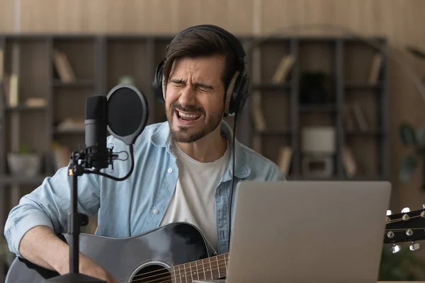 Close up man in headphones singing in microphone, playing guitar — Stock Photo, Image