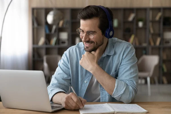 Close up smiling man in headphones using laptop, taking notes — Stock Photo, Image