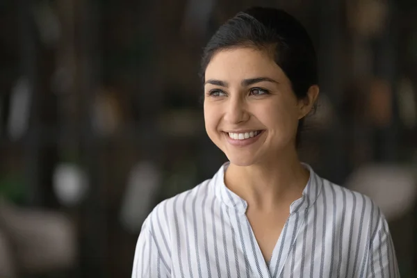 Head shot smiling dreamy Indian woman looking to aside