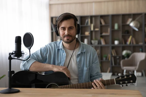 Portrait man in headphones holding guitar, sitting in home studio — Stock Photo, Image