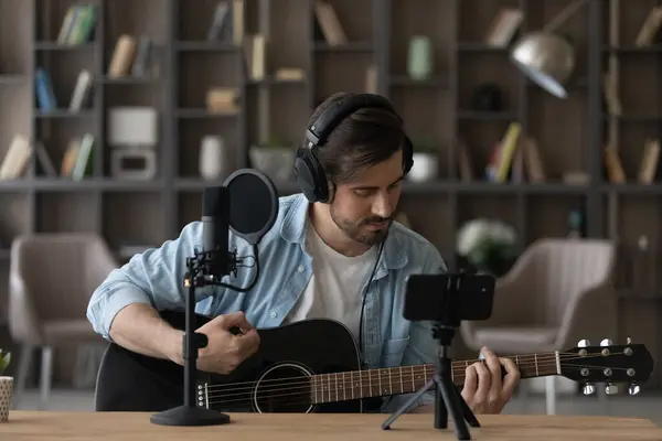 Man in headphones playing acoustic guitar, recording video on smartphone — Stock Photo, Image
