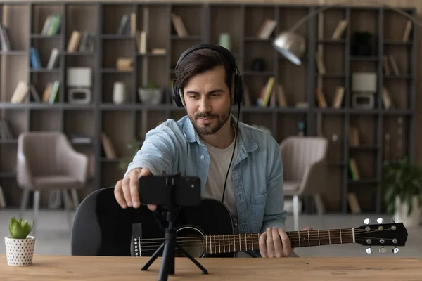 Man in headphones holding acoustic guitar, recording video on smartphone — Stock Photo, Image