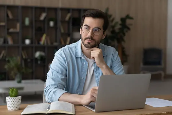 Thoughtful dreamy businessman in glasses sitting at desk with laptop — Stock Photo, Image