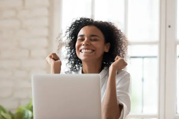Überglücklich lächelnder junger afrikanischer Ethnicity-Mitarbeiter feiert Online-Erfolg. — Stockfoto