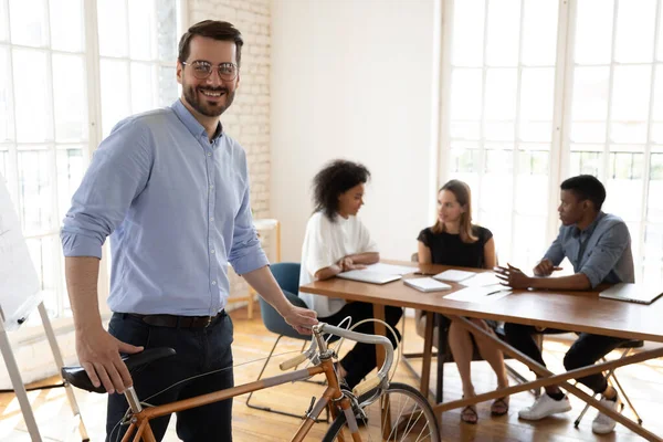 Happy young manager in eyeglasses holding bicycle, looking at camera.