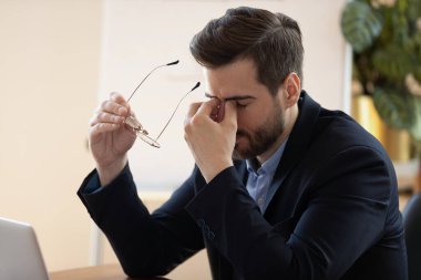 Şaşkına dönmüş genç erkek menajer gözlüklerini çıkarıyor..