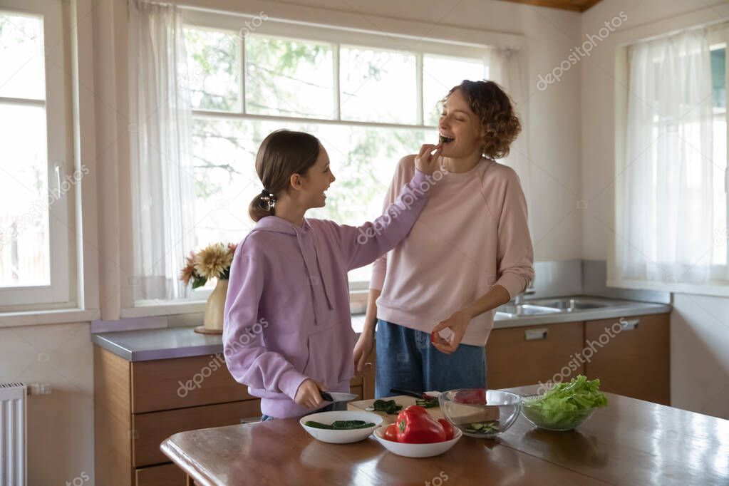 Smiling young teen girl cooking with mom in kitchen.