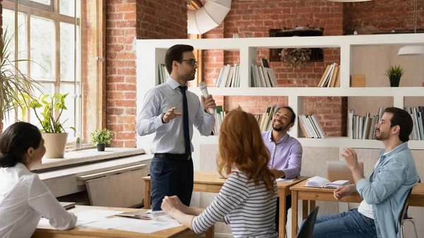 Confiado mentor de hombre de negocios sosteniendo micrófono, dirigiendo la reunión informativa con diversos empleados — Foto de Stock