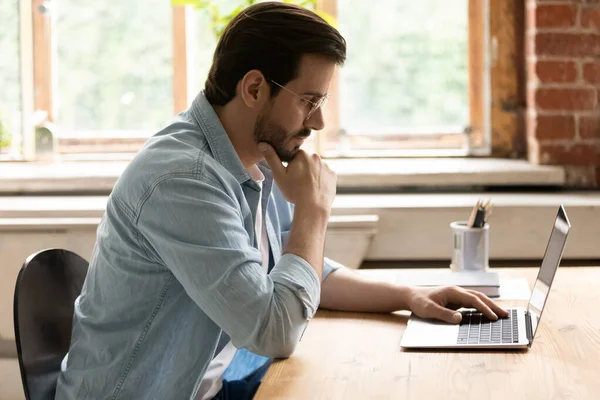 Tampilan samping pengusaha bijaksana berkacamata melihat layar laptop — Stok Foto