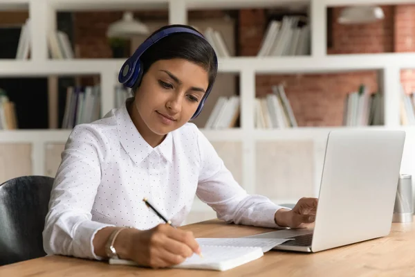 Close up motivated interested Indian woman in headphones taking notes — Stock Photo, Image