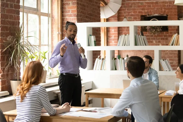 Selbstbewusster afroamerikanischer Geschäftsmann hält Mikrofon in der Hand und leitet Briefing mit Mitarbeitern — Stockfoto