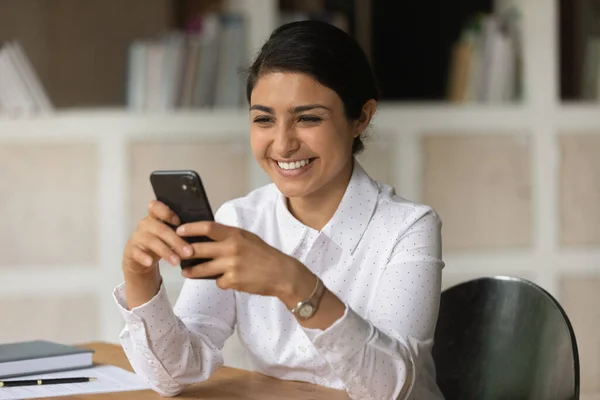 Boldog indiai üzletasszony néz smartphone képernyő, ül az asztalnál — Stock Fotó