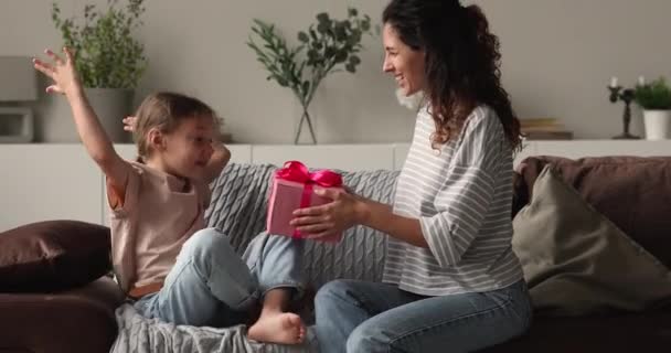 Улыбаясь, любящая молодая мамочка дарит подарок маленькой дочке. — стоковое видео