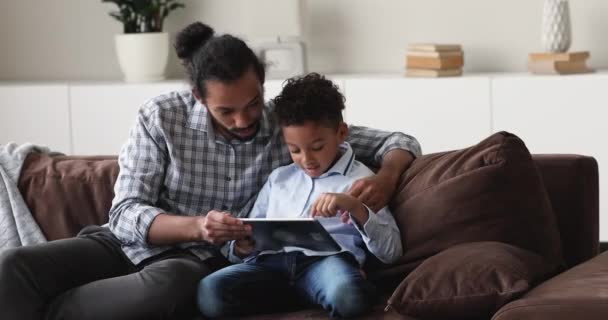 Молодой африканский любящий отец учит сына с помощью современных планшетов — стоковое видео