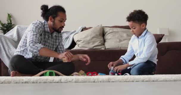 Afrikanischer Vater und Sohn spielen Spielzeugeisenbahn auf Teppich — Stockvideo