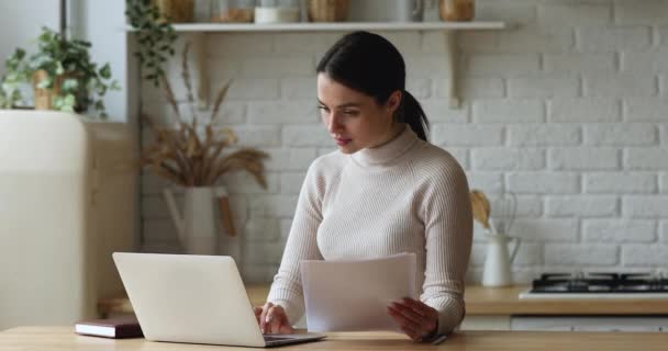 Vrouw doet papierwerk werken op laptop thuis — Stockvideo