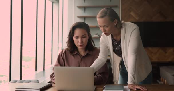 Жінки-колеги, які використовують ноутбук, працюють разом над спільним завданням — стокове відео