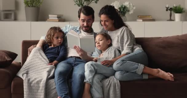 Feliz cuidado padres jóvenes lectura de libro a los niños. — Vídeos de Stock