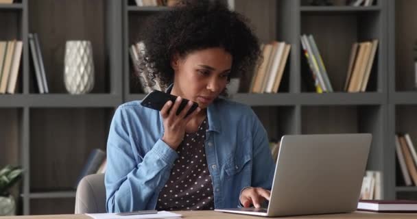 Mujer africana uso portátil sosteniendo teléfono inteligente hablando en speakerphone — Vídeo de stock