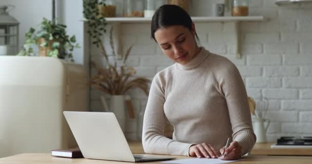 Frau, die mit Laptop im Internet surft, macht Notiz auf Papierbogen — Stockvideo