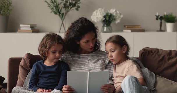 Заботливая молодая мама читает книжки маленьким детям. — стоковое видео