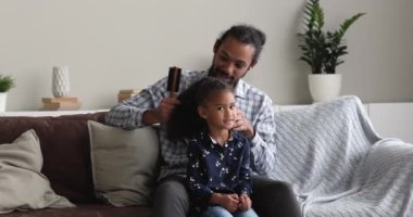 Küçük kızının kıvırcık saçlarını tarayan Afrikalı bir baba.