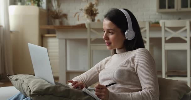 Kadın elektronik kulaklık takıyor, uzaktan bilgisayar ve video kullanarak öğreniyor. — Stok video