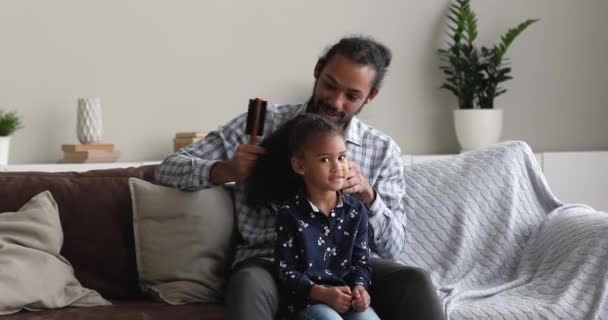 Zorgzame Afrikaanse vader kammen krullend haar van zijn kleine dochter — Stockvideo