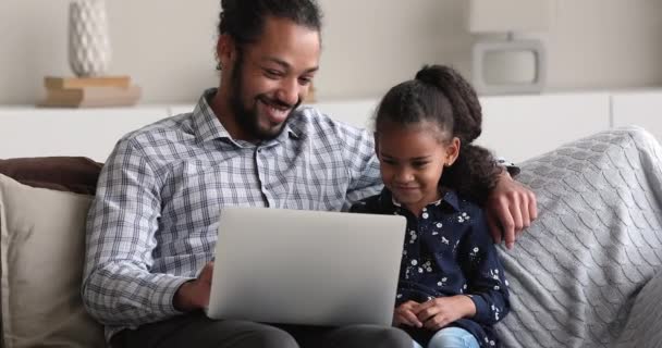 Африканський тато і маленька дитина за допомогою ноутбука сидять на дивані. — стокове відео