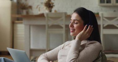 Kanepede dizüstü bilgisayarla dinlenen kadın kulaklık takıyor ve müzik dinliyor.