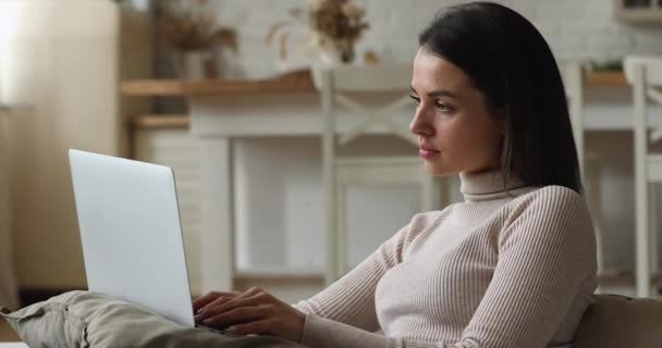 Jonge pensive vrouw zitten op de bank werken op laptop — Stockvideo