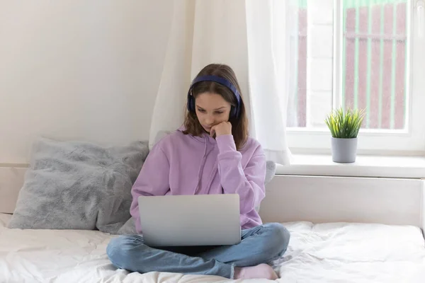 Ragazza adolescente riflessivo in cuffie wireless utilizzando il computer. — Foto Stock