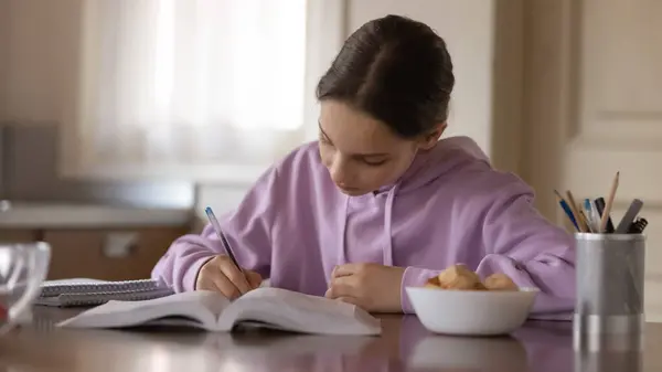 Adolescente joven concentrada estudiando sola en la cocina moderna. —  Fotos de Stock