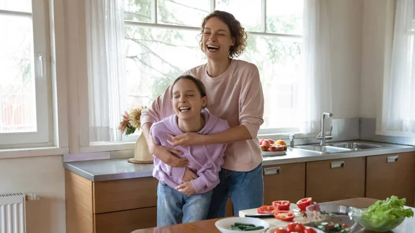 Gelukkig jong moeder having plezier met tiener dochter in keuken. — Stockfoto