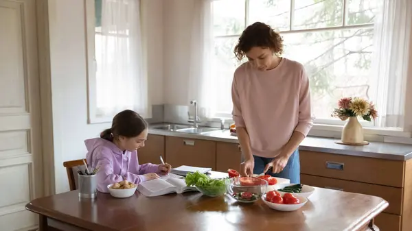 Молодая женщина готовит, пока дочь-подросток учится дома. — стоковое фото