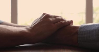 Yetişkin oğul, yaşlı babanın ellerine dokunur, yakından bakar.