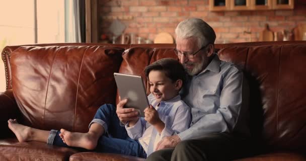 Farfar kramar lilla sonson slappna av på soffan med tablett gadget — Stockvideo