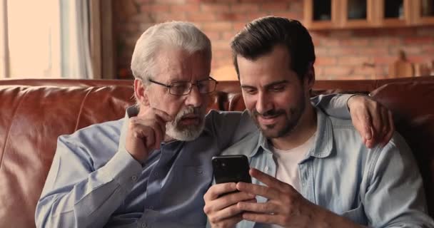 Anciano hombre su hijo adulto leer noticias fantásticas en el teléfono inteligente — Vídeo de stock