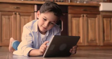 Küçük çocuk yerde tek başına yatıyor. Tablet oyunu oynuyor.