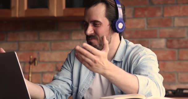 Młody mężczyzna nosi słuchawki rozmawiać z klientem przez połączenie wideo — Wideo stockowe