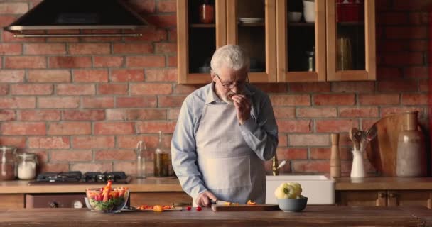 Oudere man draagt schort koken alleen in de keuken — Stockvideo