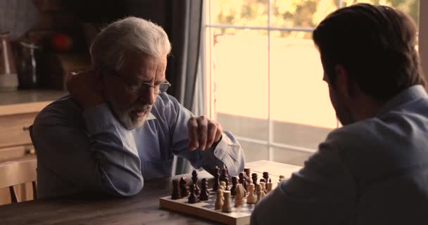 Grave pensionista papá jugar ajedrez con adulto hijo en casa — Vídeos de Stock