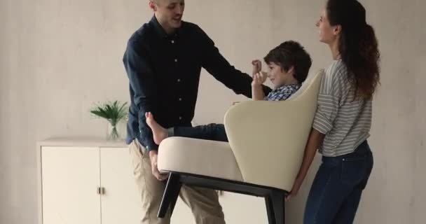 Les parents portent une chaise confortable où leur petit fils est assis — Video