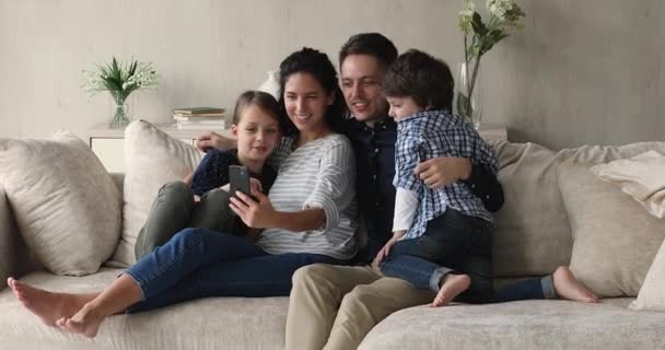 Paar en kinderen genieten van grappige mobiele applicatie zittend op de bank — Stockvideo