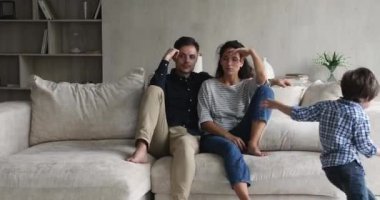 Çocuklar kanepede oturan bezgin ailelerin etrafında koşuşturuyorlar.