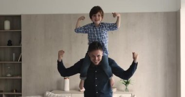 Güçlü bir adam oğlunu omuzlarında tutuyor ve pazılarını gösteriyor.